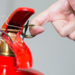 Close-,Up,Fire,Extinguisher,And,Pulling,Pin,On,Red,Tank.